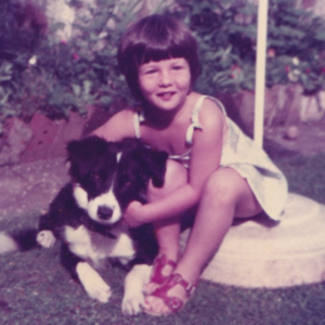 Old faded colour photo of a young girl hugging a pet dog in a garden.